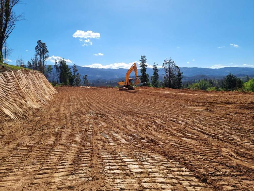 Excavadora sobre un terreno con movimientos de tierra ya realizados, con cordillera al fondo