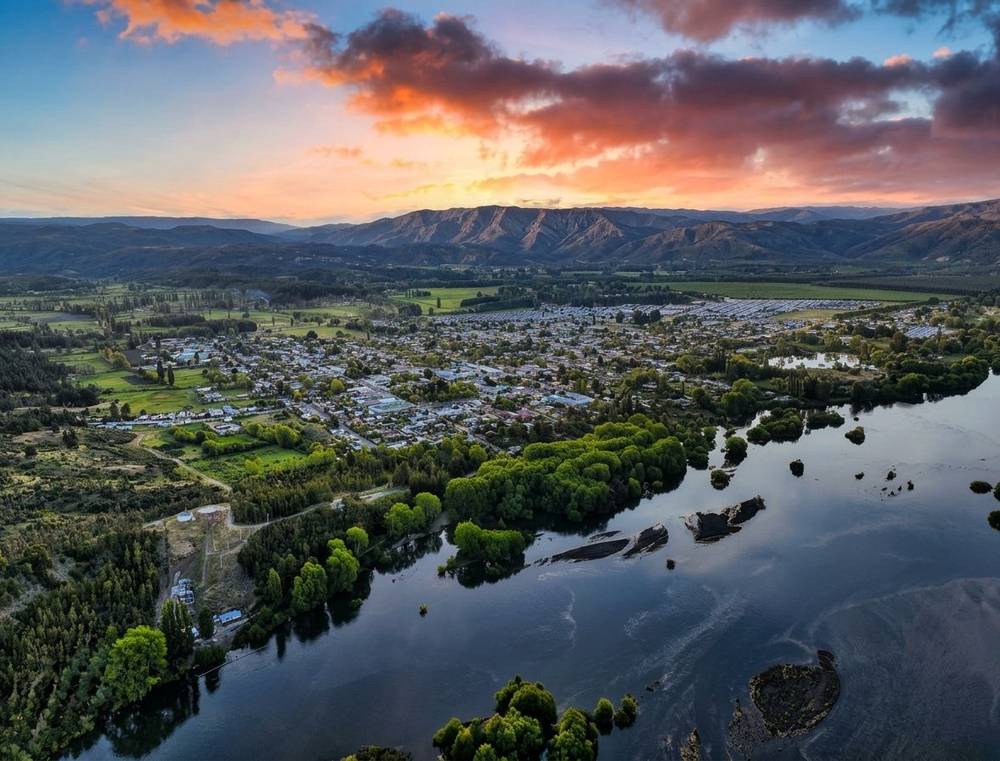 Vista aérea de un pueblo junto a un río, con cerros al fondo al atardecer